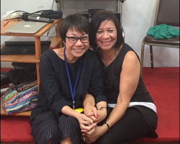 Two women sitting close together on the floor of a training room