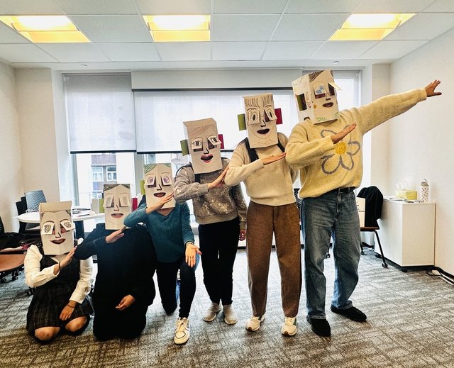 Participants wearing decorated paper boxes on their heads and posing in a meeting room