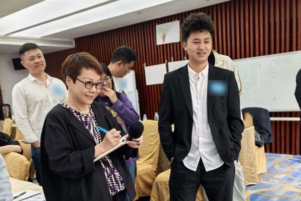 A trainer with a microphone and clipboard listening to a participant during a workshop