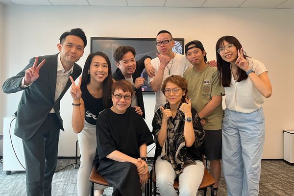 A group of smiling workshop participants posing with peace signs and thumbs up in a meeting room
