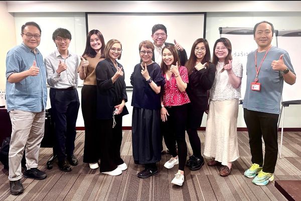 A group of smiling workshop participants giving a thumbs up in a training room