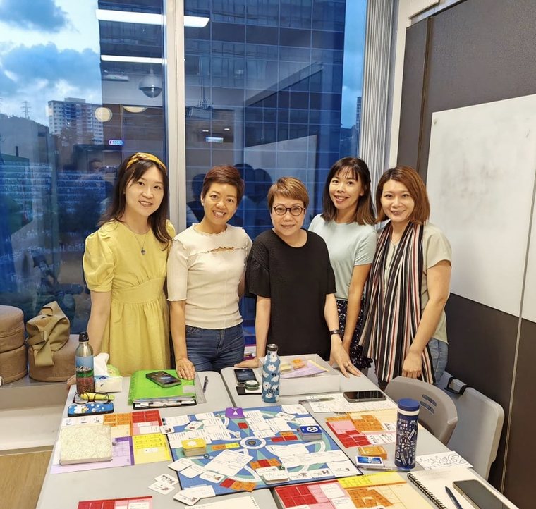 Five women standing around a Transformation Game board