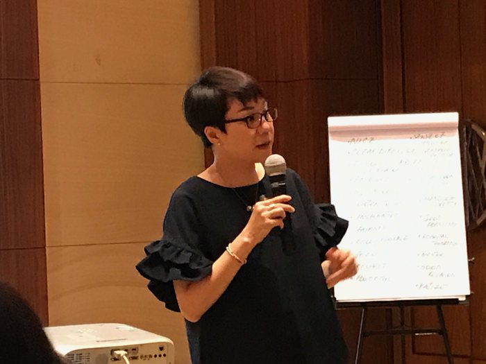 A trainer speaking with a microphone next to a flipchart during a workshop