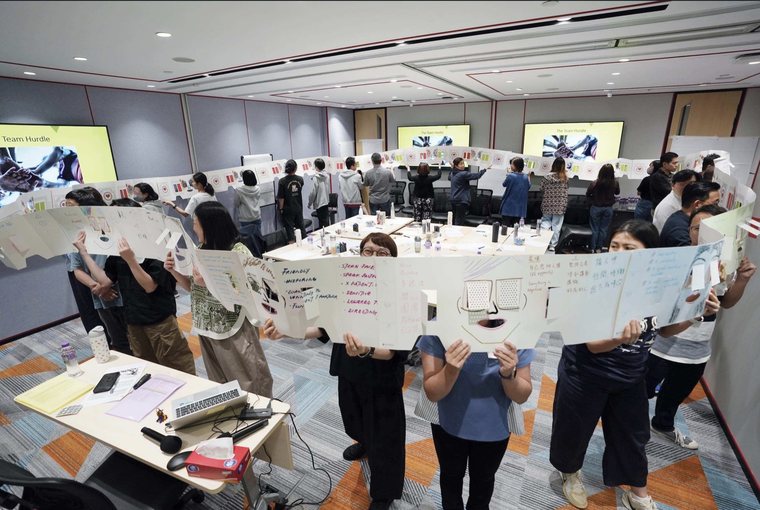 Participants holding long unfolded paper box faces across a training room