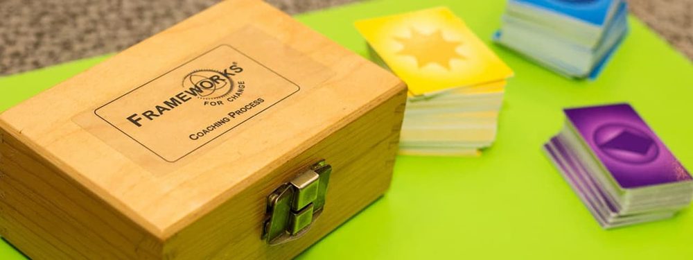 Wooden Frameworks for Change Coaching Process box beside stacks of yellow, blue and purple cards on a green table