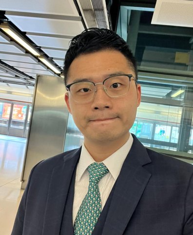 Portrait of Danny Lau wearing glasses and a navy suit with a green patterned tie