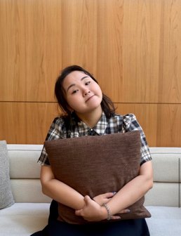 Portrait of Shiny Lai smiling and holding a brown cushion on a sofa