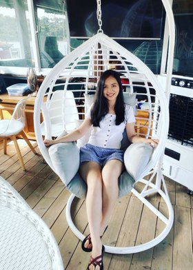 Portrait of Serena smiling while sitting in a white hanging egg chair on a wooden deck