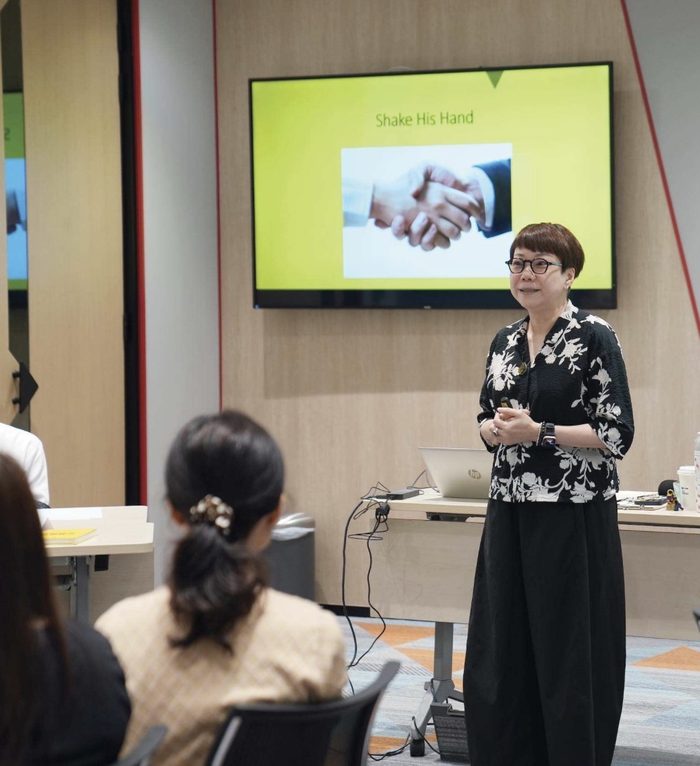 A trainer standing beside a screen showing a handshake picture while seated participants listen